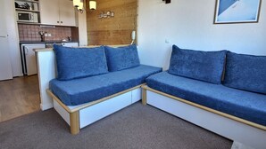 Ein modernes Wohnzimmer mit einem Ecksofa, einer Wandvertäfelung aus Holz, einer Küchenzeile und einem gerahmten Poster.