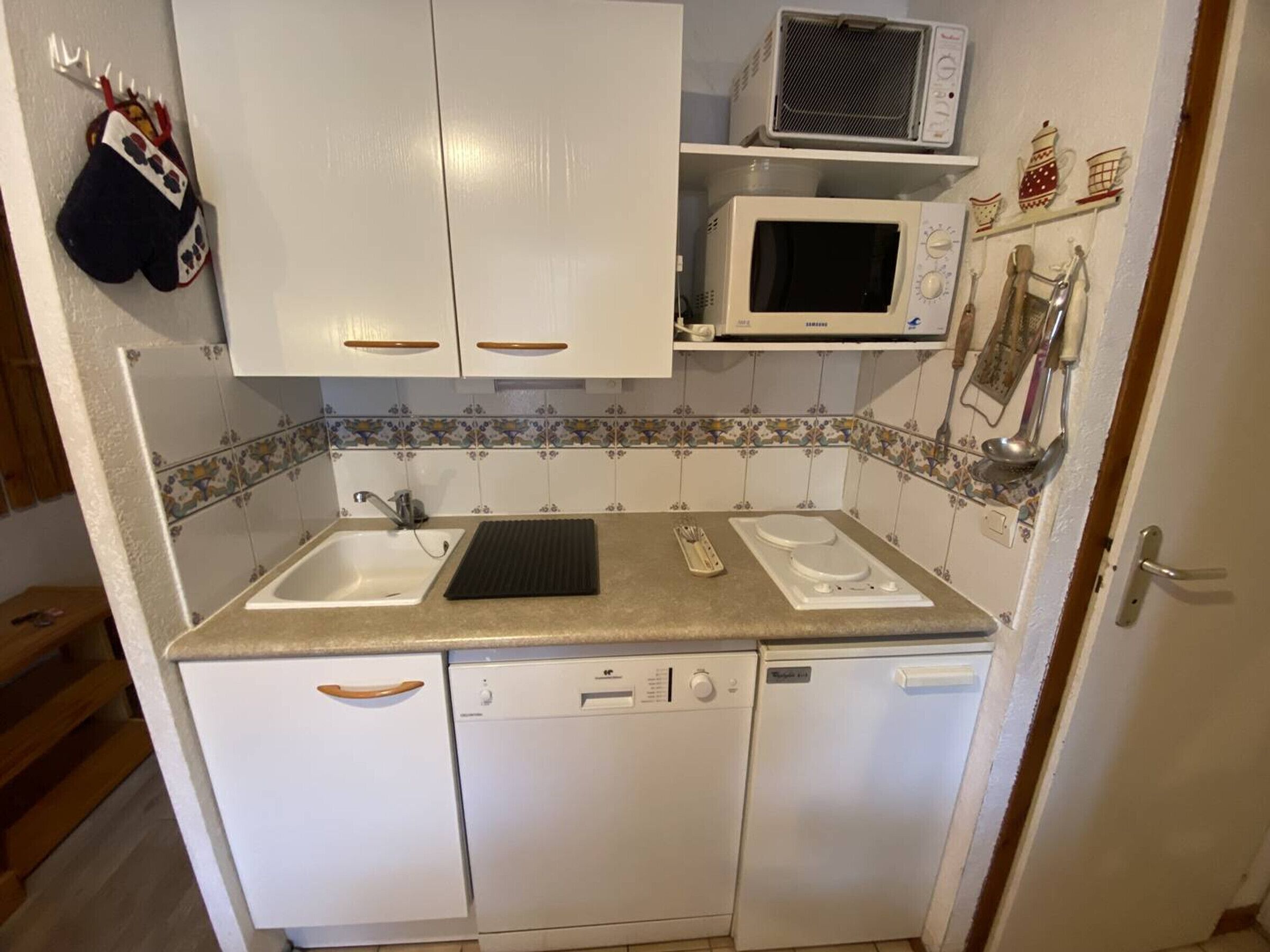 A compact kitchen with white cabinets, a microwave, a sink, and a dishwasher.
