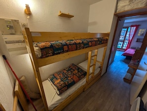 A bunk bed with a patterned quilt, a wooden shelf, and a wall-mounted heater.