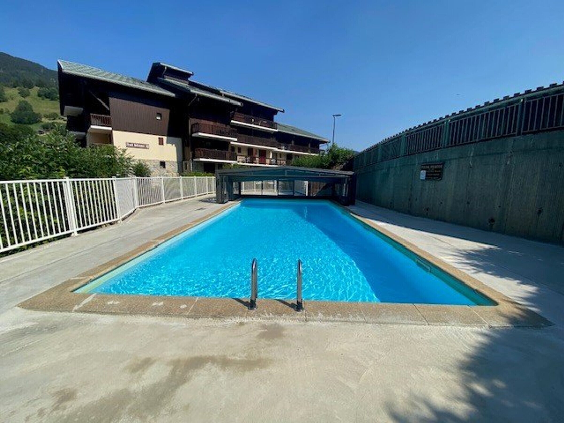 Una piscina rectangular con un trampolín en el centro, rodeada por una terraza de hormigón.