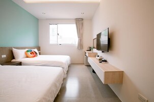 Habitación de hotel con dos camas, televisión, un escritorio pequeño y una ventana con cortinas.