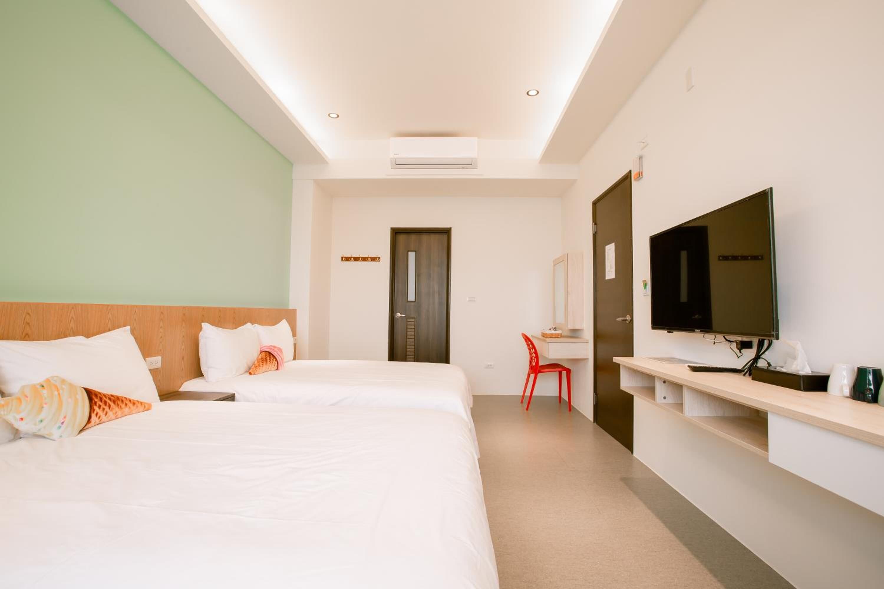 A hotel room with two beds, a desk, a TV, and a red chair.