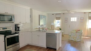 Una cocina moderna con gabinetes blancos, microondas, horno, cafetera y lavavajillas.