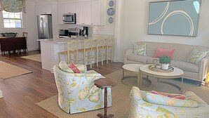 Una sala moderna con sofás de estampado floral, una mesa de centro y un comedor con una cocina al fondo.