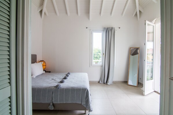 A bedroom with a bed, a window with curtains, a mirror, and a door leading to an outdoor area. - Charming House, Life is Good in Sxm (Saint Martin)