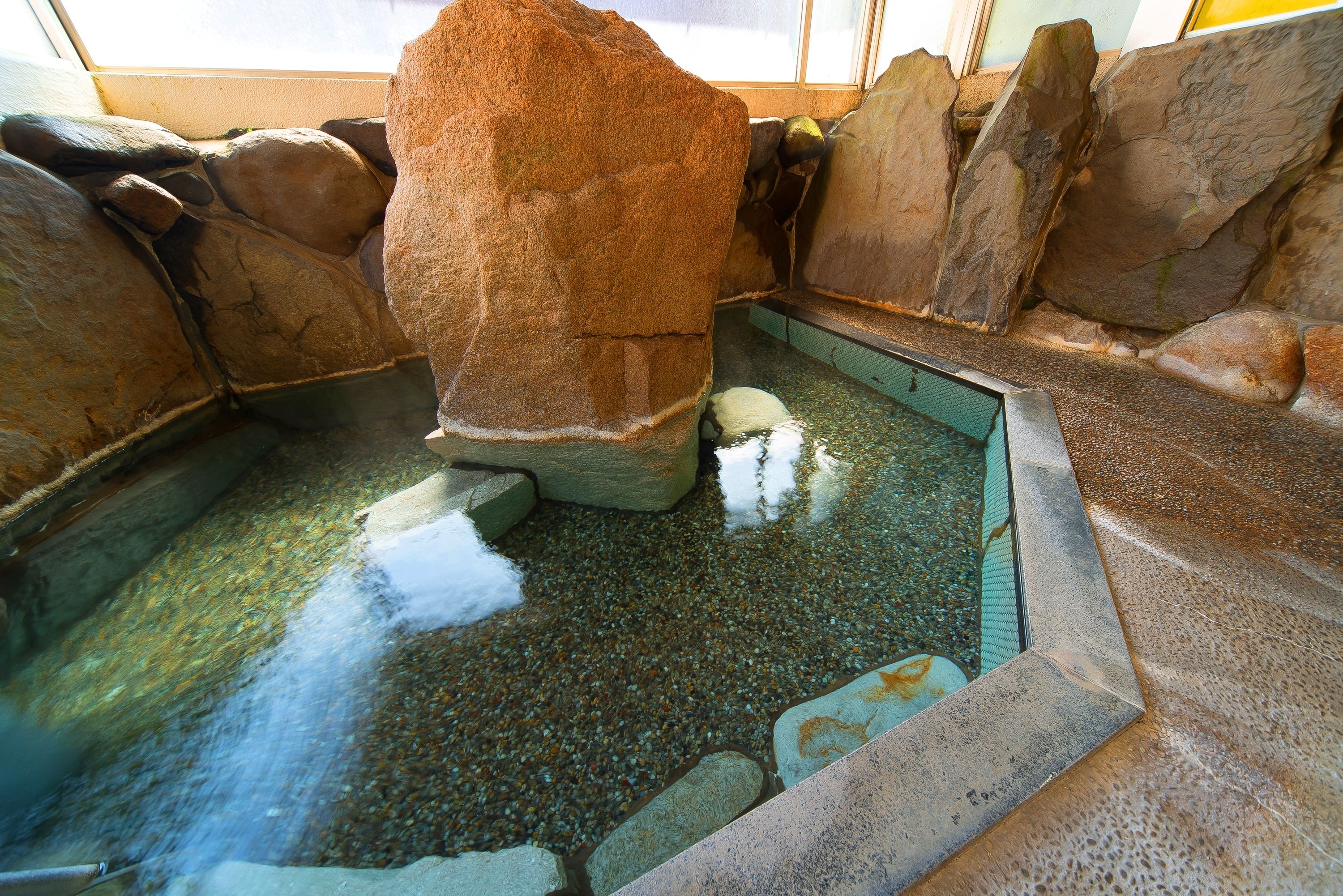 Un área de aguas termales con rocas grandes y piso cubierto de guijarros.