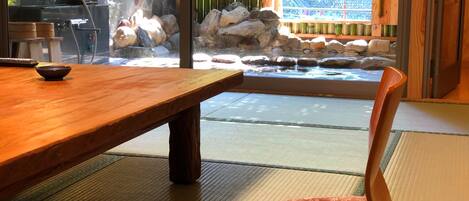 A traditional Japanese room with tatami flooring, a wooden table, and a view of a rock garden through a sliding door.