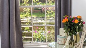 A window with a view of a garden, a vase with flowers, and a small table with a box and a picture frame.