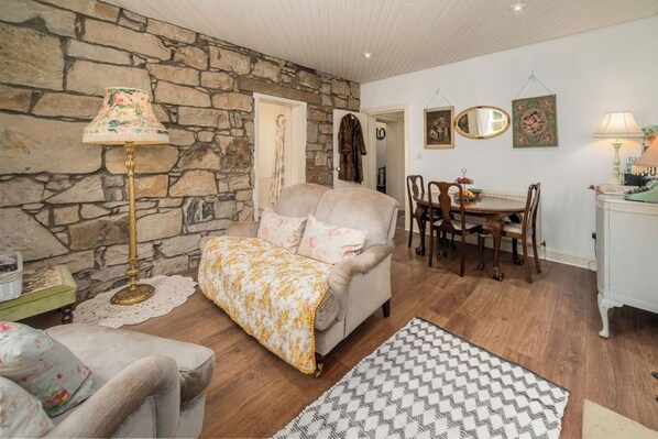 A cozy living room with a stone wall, a sofa, a dining table with chairs, and a lamp.