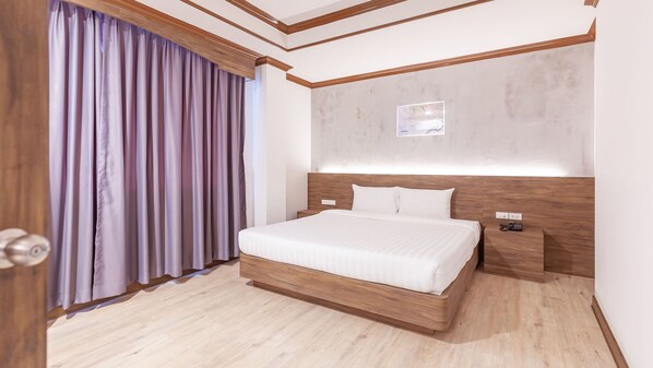 A modern hotel room with a large bed, wooden headboard, and a nightstand with a phone.