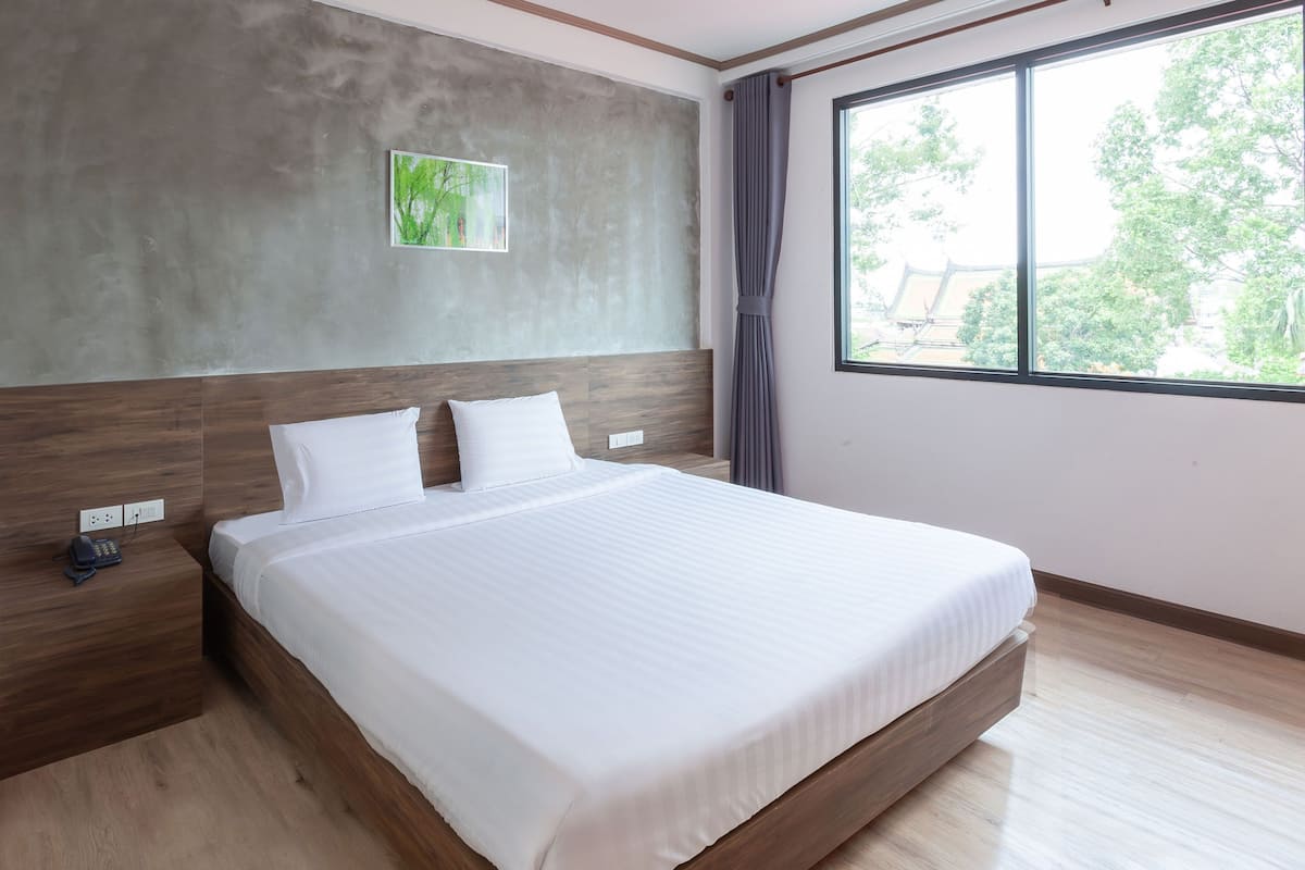 A modern hotel room with a large bed, a wooden headboard, a grey accent wall, a small picture, and a window with curtains.