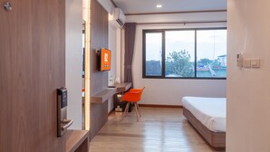 Ein modernes Hotelzimmer mit einem Bett, einem Schreibtisch mit Stuhl, einem Fernseher und einem Fenster mit Blick auf Gebäude und Bäume.