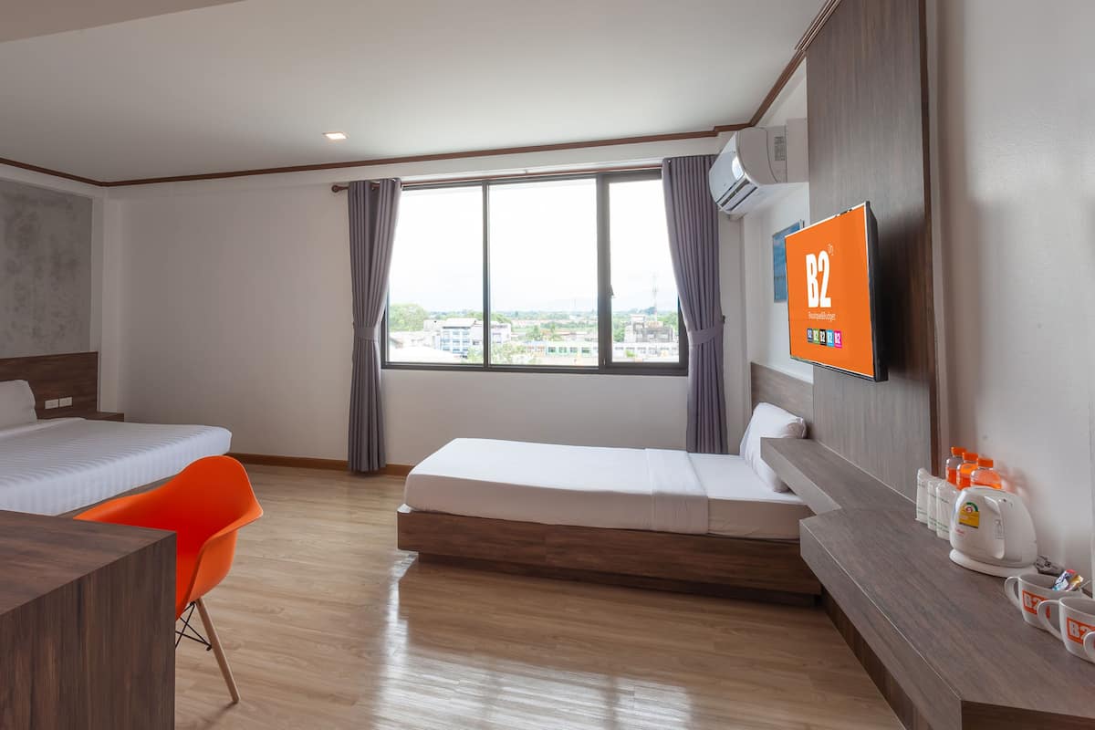 A hotel room with two single beds, a desk, a chair, a TV, and a window with curtains.