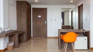 Ein Hotelzimmer mit Holzboden, einem Schreibtisch mit Stuhl, einer kleinen Kühlbox und einem Spiegel.
