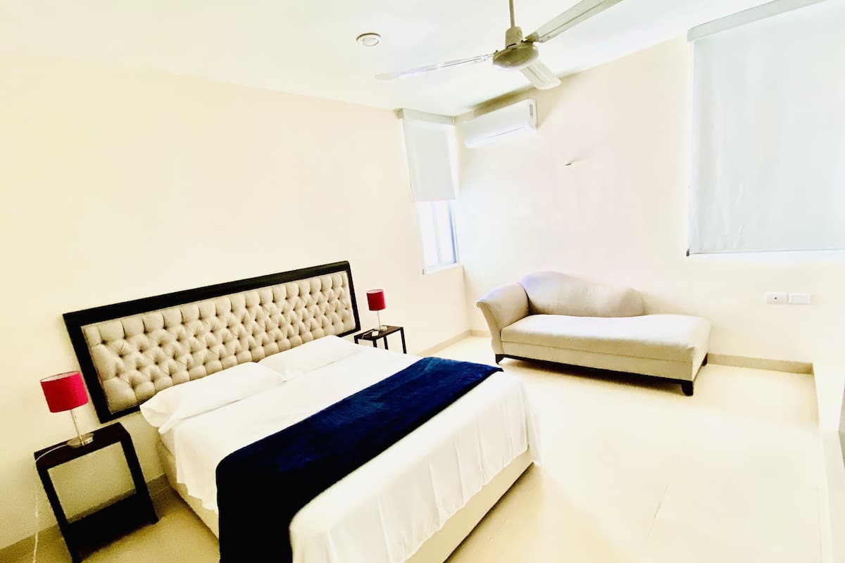 A bedroom with a bed, bedside tables, a ceiling fan, a window, and a sofa.