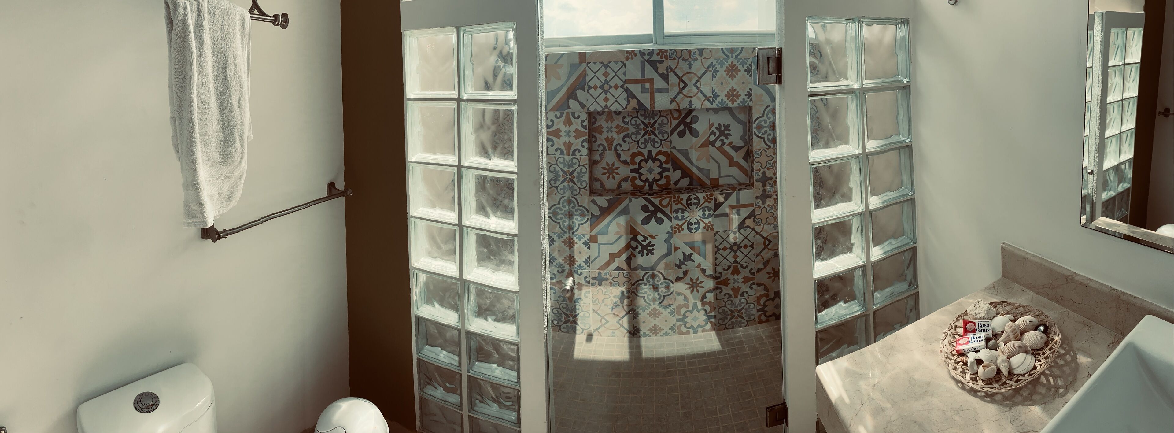 A bathroom with a toilet, a towel rack, a glass shower enclosure, and a vanity with a basket of toiletries.