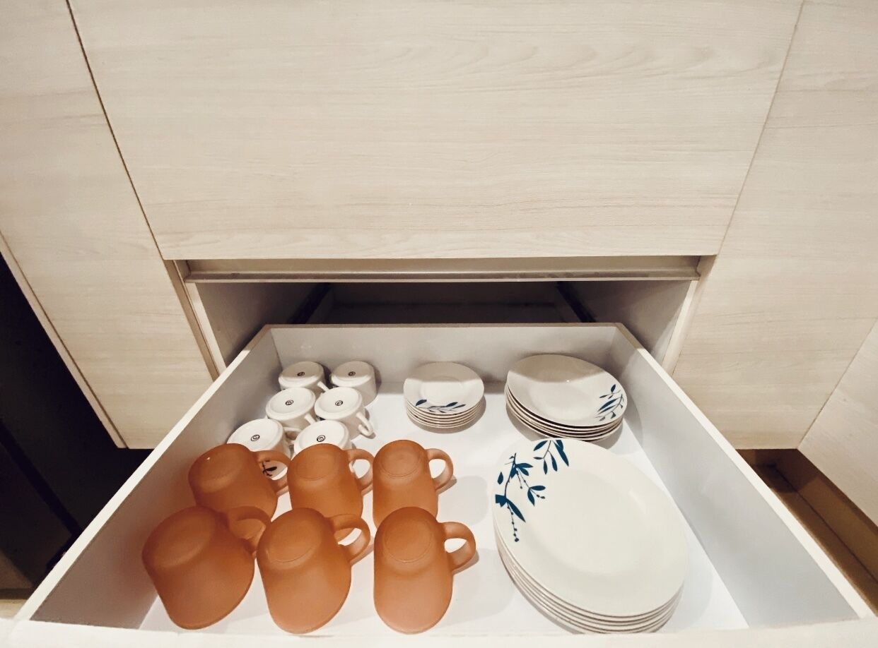 Un cajón con utensilios de cocina ordenados, incluyendo tazas, platos y tazones.