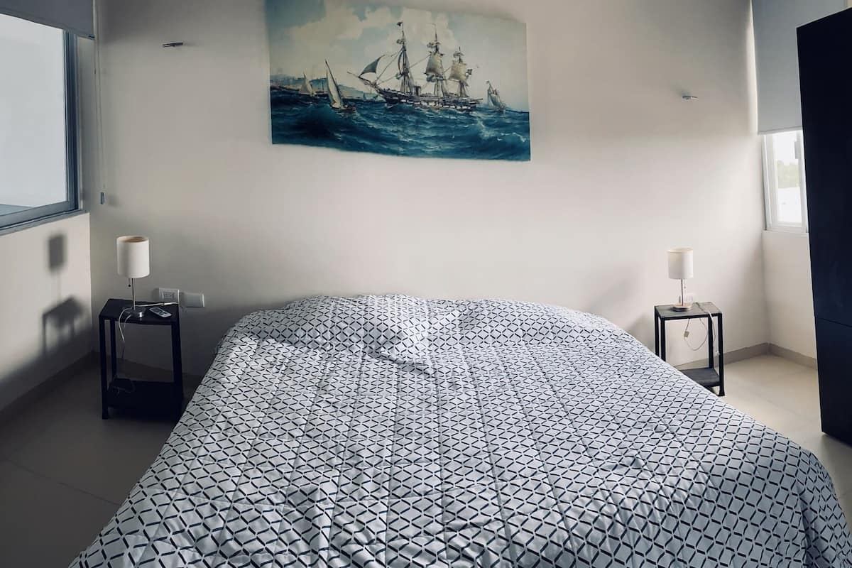A bedroom with a bed, a nightstand, a lamp, a wardrobe, and a painting of a ship on the wall.