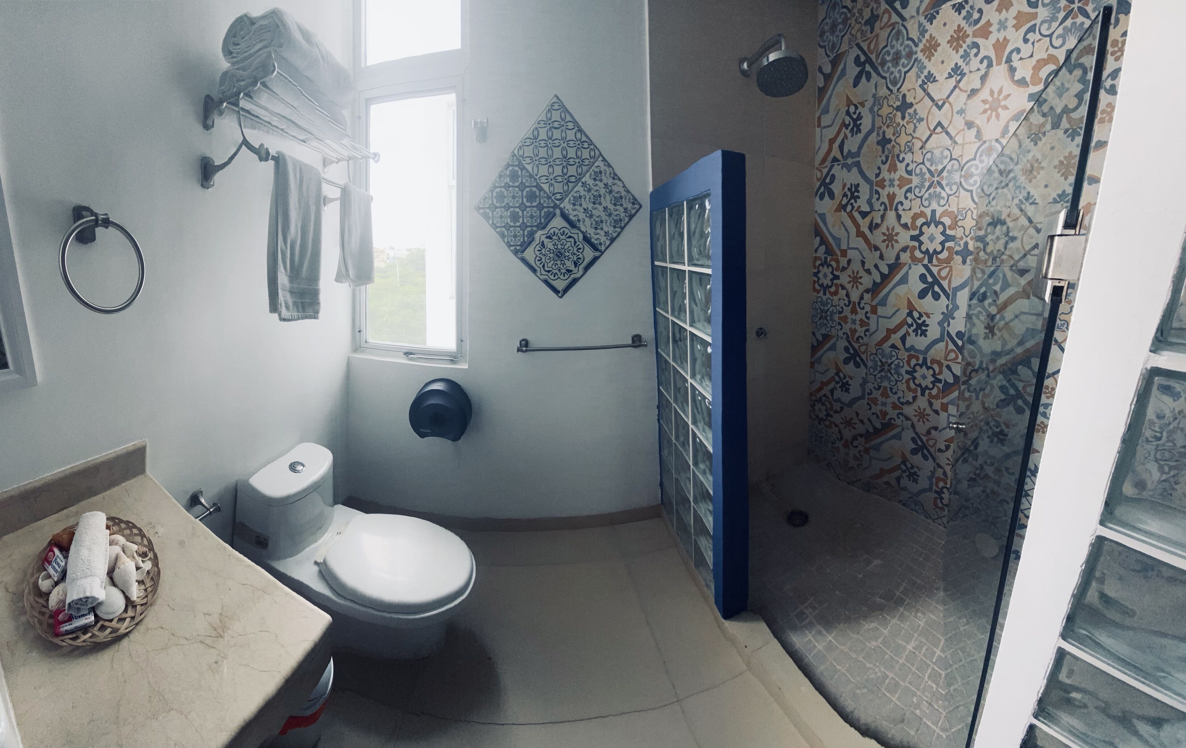 A bathroom with a toilet, a towel rack, a shower, and a patterned tile wall.
