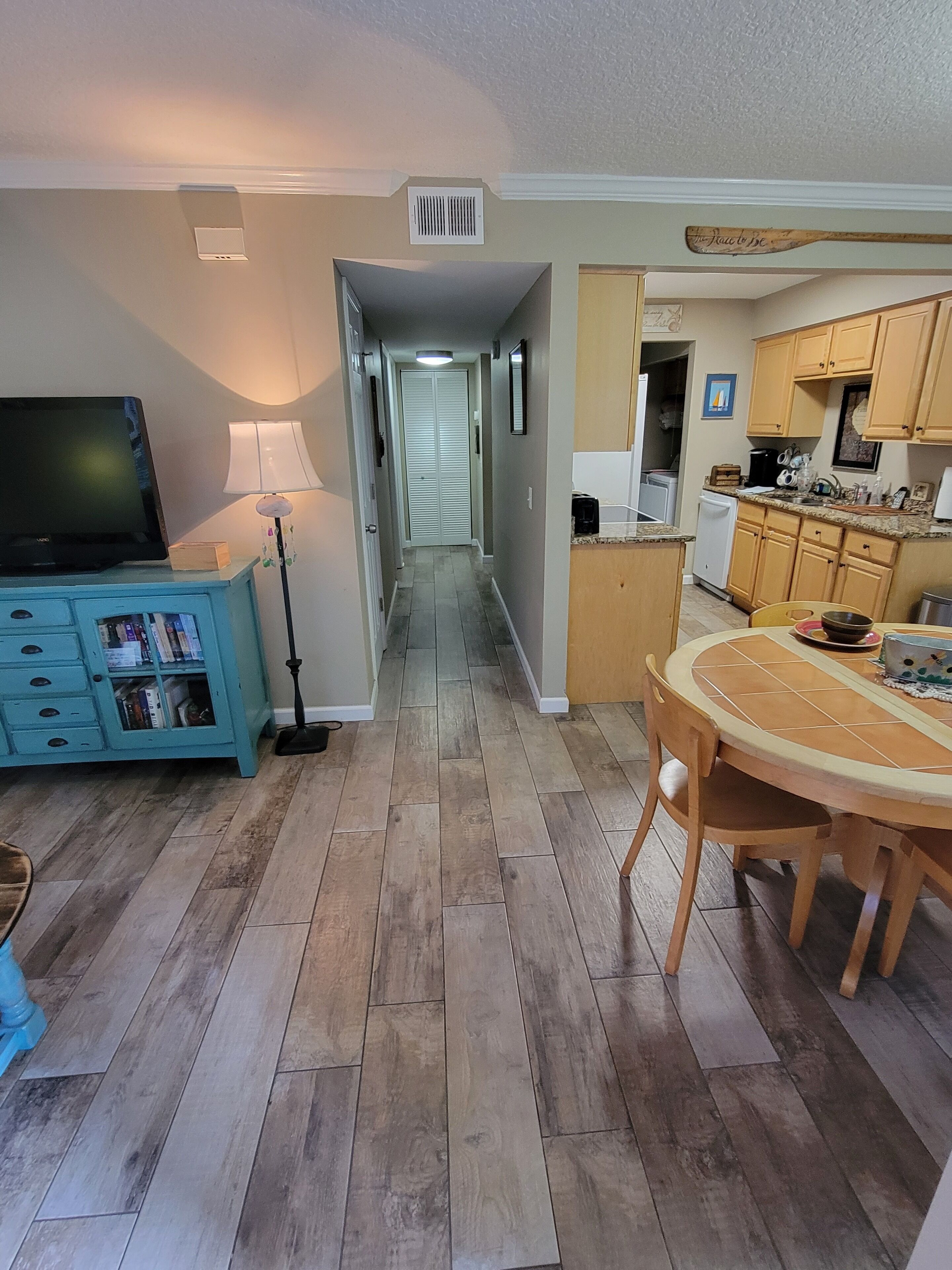 A modern kitchen with wooden cabinets, a dining table, and a TV in the living area.