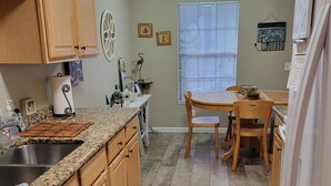 A kitchen with wooden cabinets, a granite countertop, a sink, a dining table with chairs, and a window with blinds. - The Place to Be !! Walk 2 Beach, Restaurants, Activities (St. Augustine)