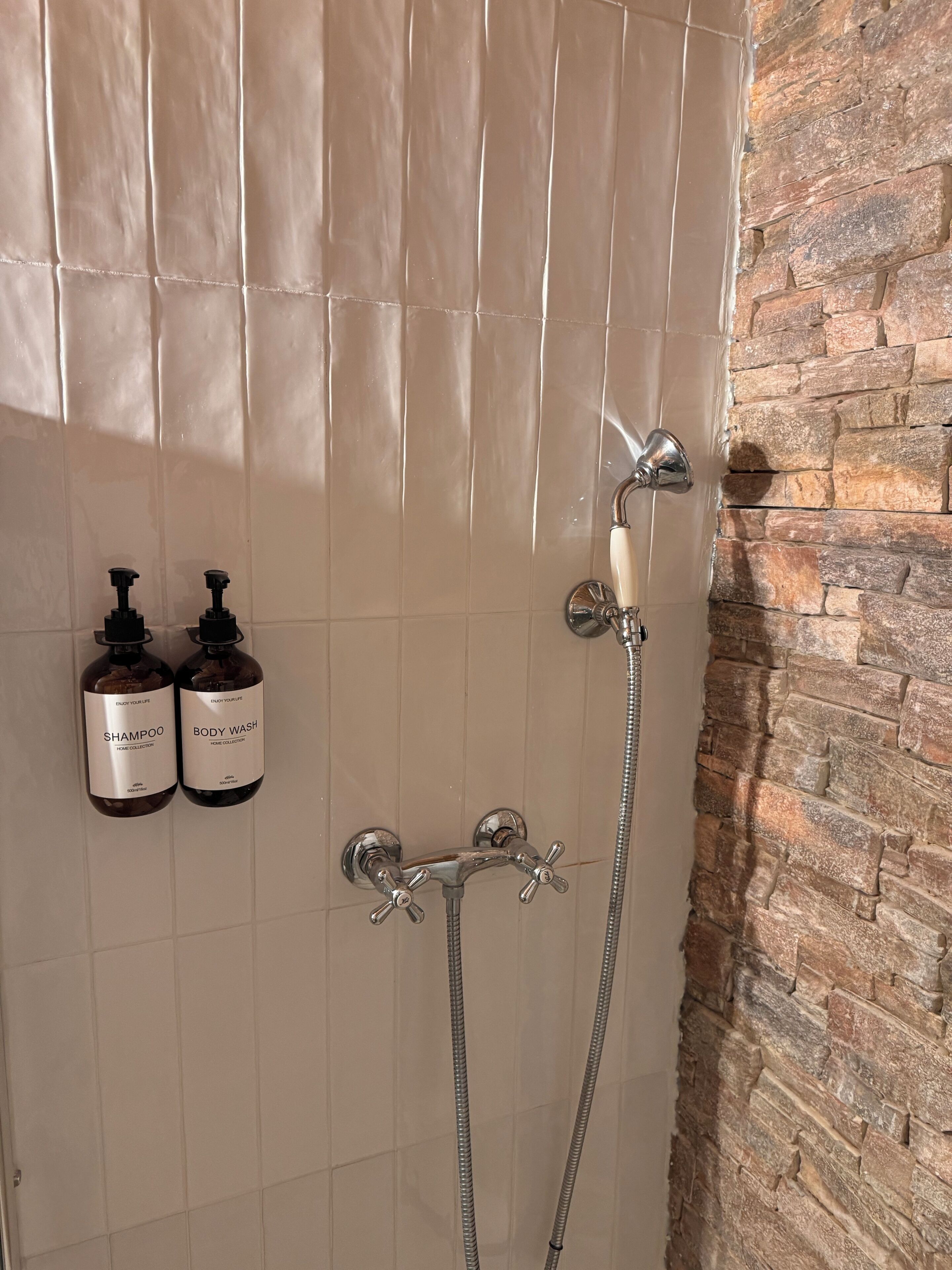 A bathroom with a shower, a tiled wall, and two bottles of shampoo and body wash.