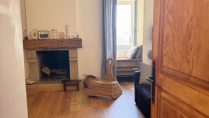 A living room with a fireplace, a wicker chair, a sofa, and a wooden door. - Atypical village apartment (Olmeto)