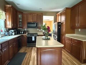 A kitchen with wooden cabinets, a microwave, stove, refrigerator, and a central island with a vase of flowers. - Beautiful Wiscasset Home 5 AC units, sleeps 16  (Wiscasset)