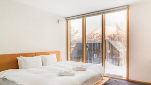 Una camera d'hotel moderna con un letto grande, una testiera in legno e vista su un paesaggio innevato attraverso finestre a tutta altezza.