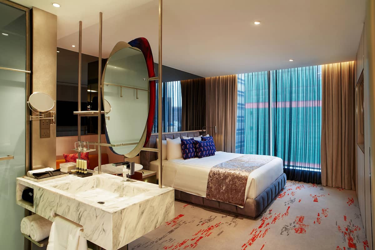 A modern hotel room with a large bed, a separate bathroom with a marble vanity, and large windows with curtains.
