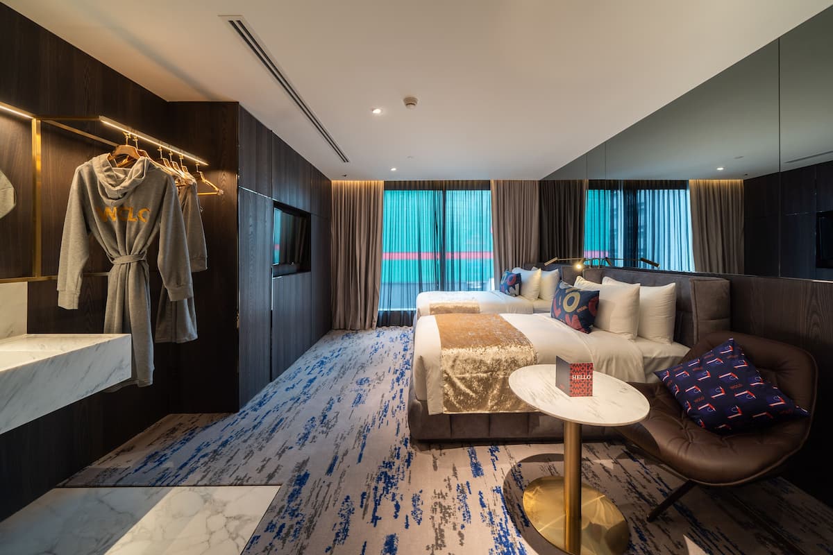 A modern hotel room with a large bed, a sitting area with a chair, a vanity with a mirror, and a robe hanging on a rack.