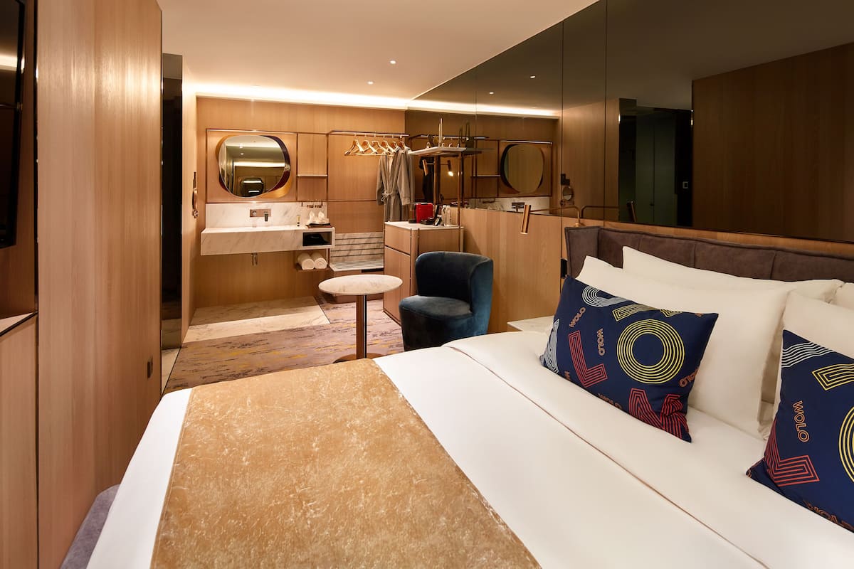 A hotel room with a bed, a desk, a chair, a mirror, and a wardrobe.