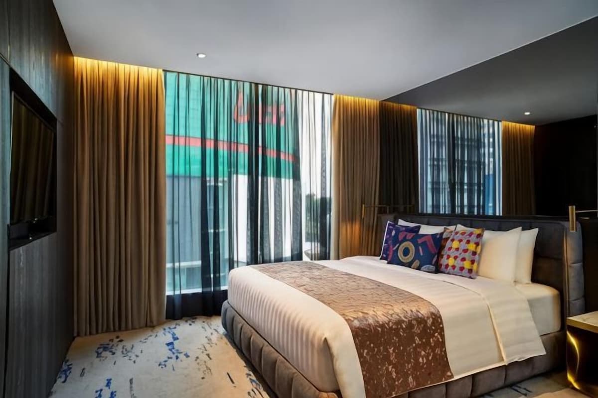 A modern hotel room with a large bed, a TV, and a view of a cityscape through the window.