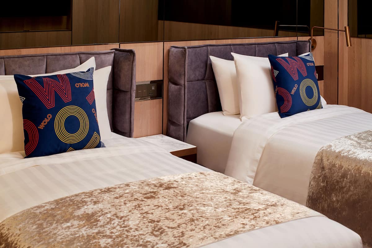 A hotel room with two beds, each with a headboard and a pillow with a colorful pattern.
