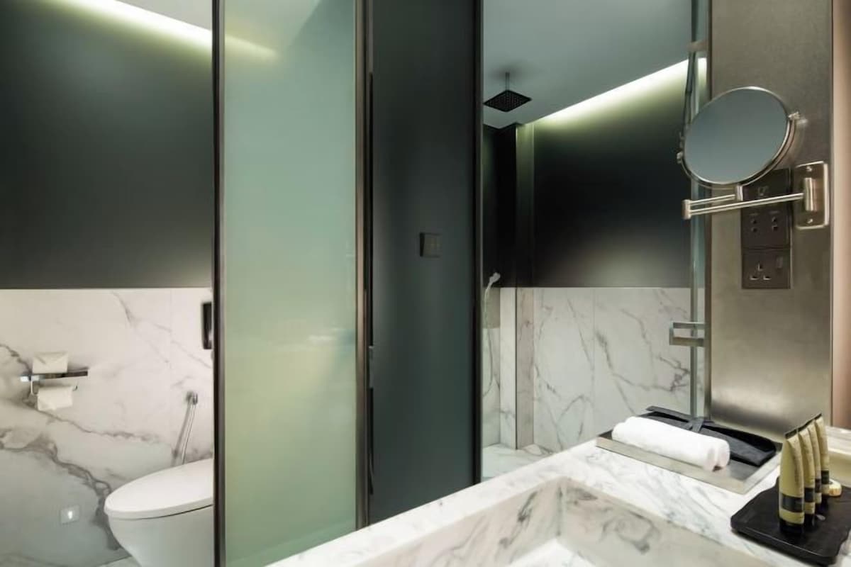 A modern bathroom with a glass shower enclosure, a marble countertop, and a round mirror.