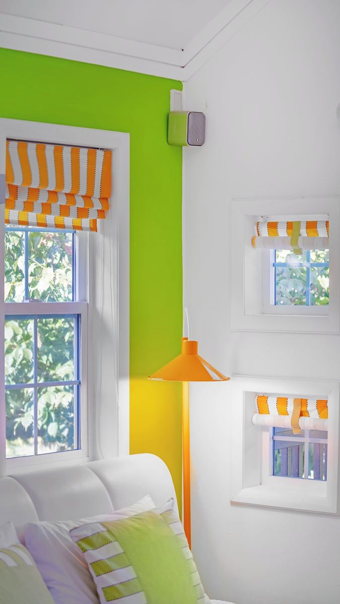Ein Zimmer mit einer weißen Couch, einer grünen Wand und einem Fenster mit orangefarbenen Vorhängen.