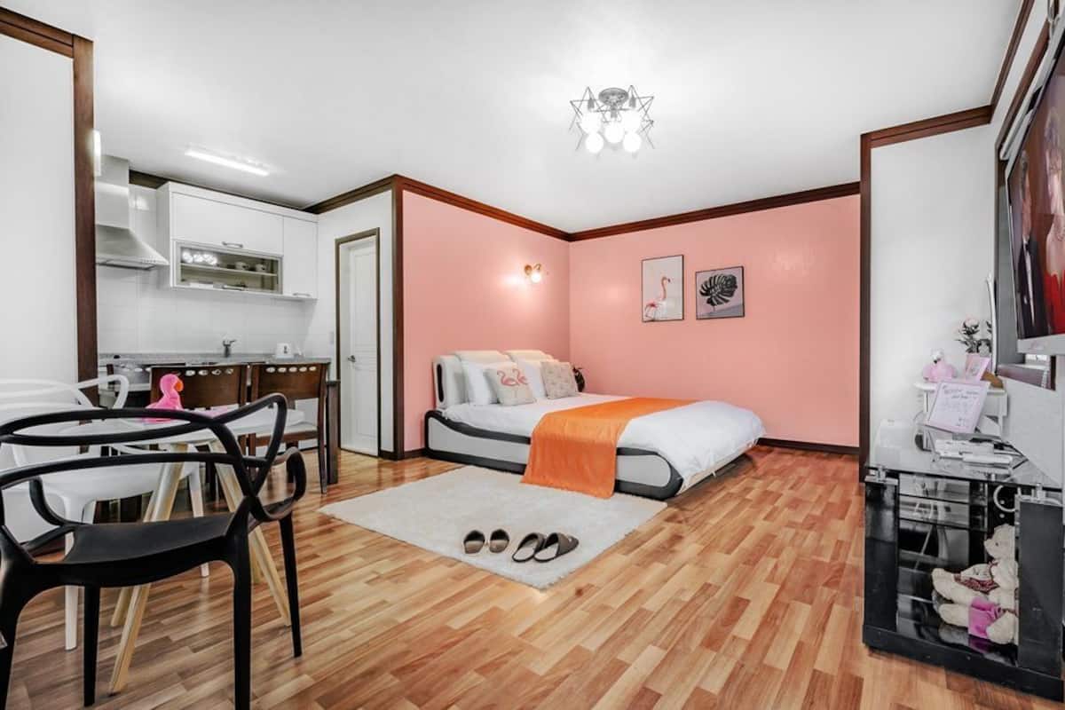 Una habitación pequeña con una cama, un escritorio, una silla, una mesita y un televisor.