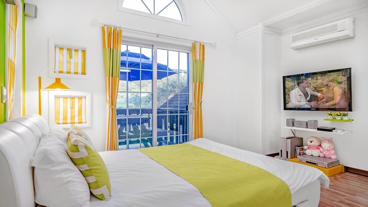A hotel room with a bed, a TV, a window with curtains, and a view of the outside.