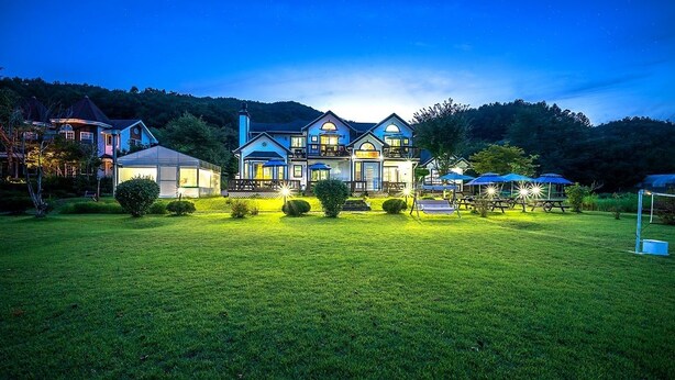 A large, multi-story house with a well-maintained lawn and outdoor seating area. - Star Sonata Pension (Hongcheon)