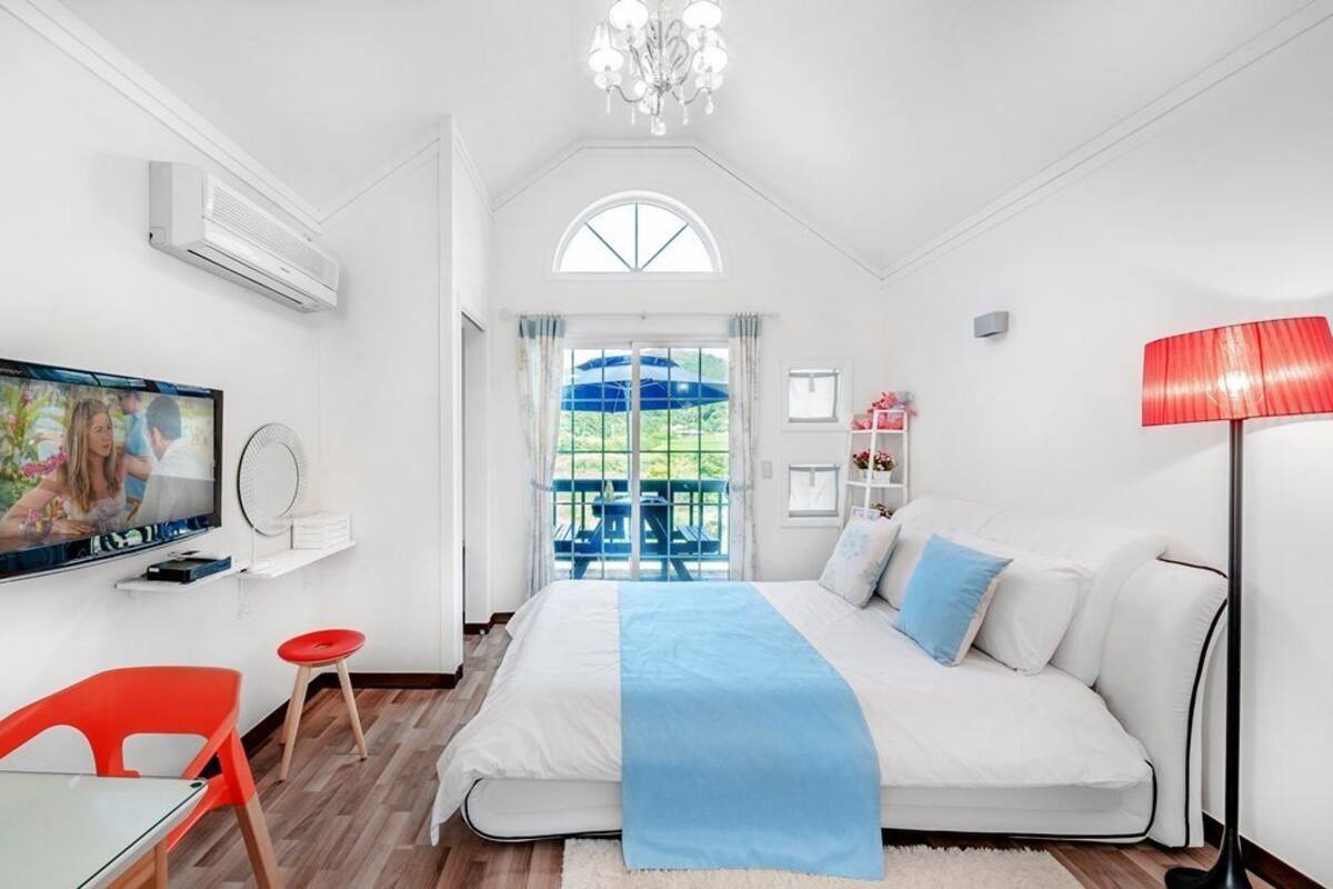 Un dormitorio moderno con una cama grande, un televisor, un comedor con sillas rojas y vistas al exterior.