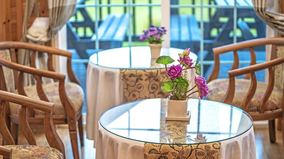 Una mesa redonda de vidrio con un centro de mesa floral, rodeada de sillas de madera con cojines estampados.