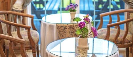 Una mesa redonda de vidrio con un centro de mesa floral, rodeada de sillas de madera con cojines estampados.