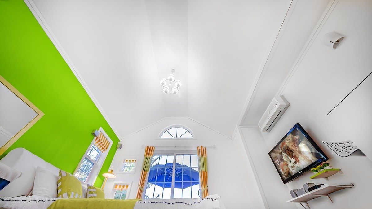 A room with a bed, a window with curtains, a ceiling light, and a wall-mounted air conditioner.