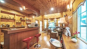 A cozy wooden cabin interior with a bar area, dining space, and a large window offering a view. - Star Sonata Pension (Hongcheon)