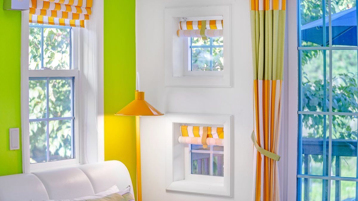 A room with a white sofa, three windows with orange and white checkered curtains, and a bright green wall.