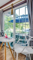 Una habitación con un ventanal grande, una silla blanca, una mesita redonda y una lámpara colgante.