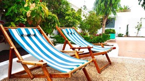 Two wooden lounge chairs with blue and white striped cushions, positioned on a pebble-tiled patio surrounded by lush greenery. - CASA VINCA, quiet holiday home near the beach (Puerto del Carmen)