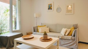 A cozy living room with a sofa, a coffee table, and a lamp. There are two framed pictures on the wall. - Joli appartement avec jardinet (Hyères)