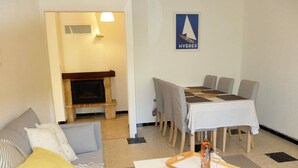 A cozy living room with a sofa, a dining table with chairs, a fireplace, and a wall-mounted sign. - Joli appartement avec jardinet (Hyères)