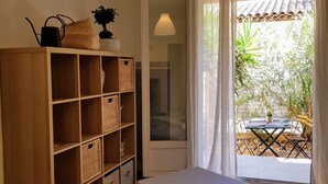A room with a wooden bookshelf, a cushioned bench, and a table outside. - Joli appartement avec jardinet (Hyères)